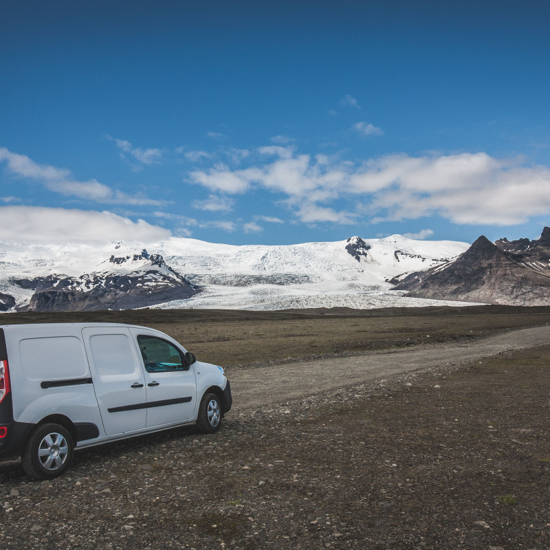Campervan vor einer Ebene, im Hintergrund Berge.
