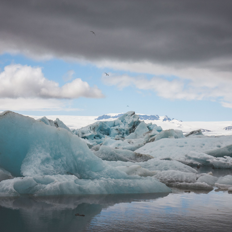 Eisschollen treiben im See, dichte Wolken am Himmel.