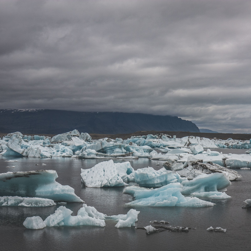 Eisschollen treiben im See, dichte Wolken am Himmel.