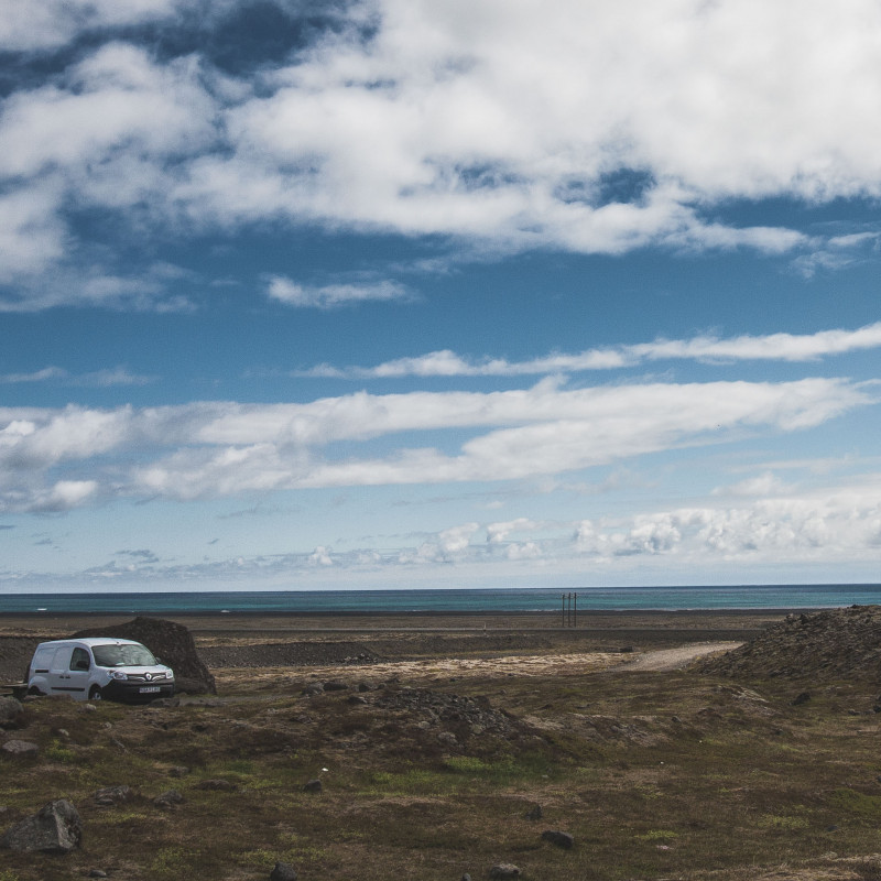 Campervan vor einer Ebene, im Hintergrund Meer.
