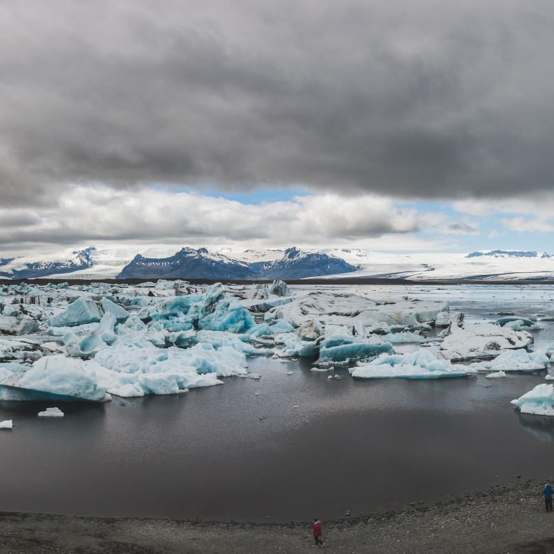 Panorama: Eisschollen treiben im See, dichte Wolken am Himmel.