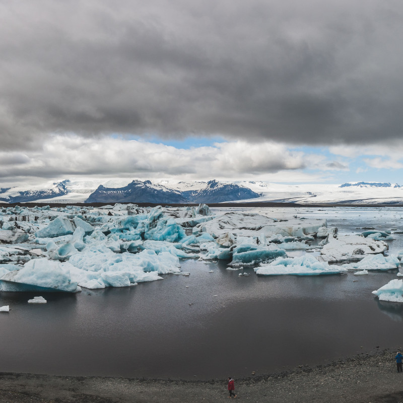 Panorama: Eisschollen treiben im See, dichte Wolken am Himmel.