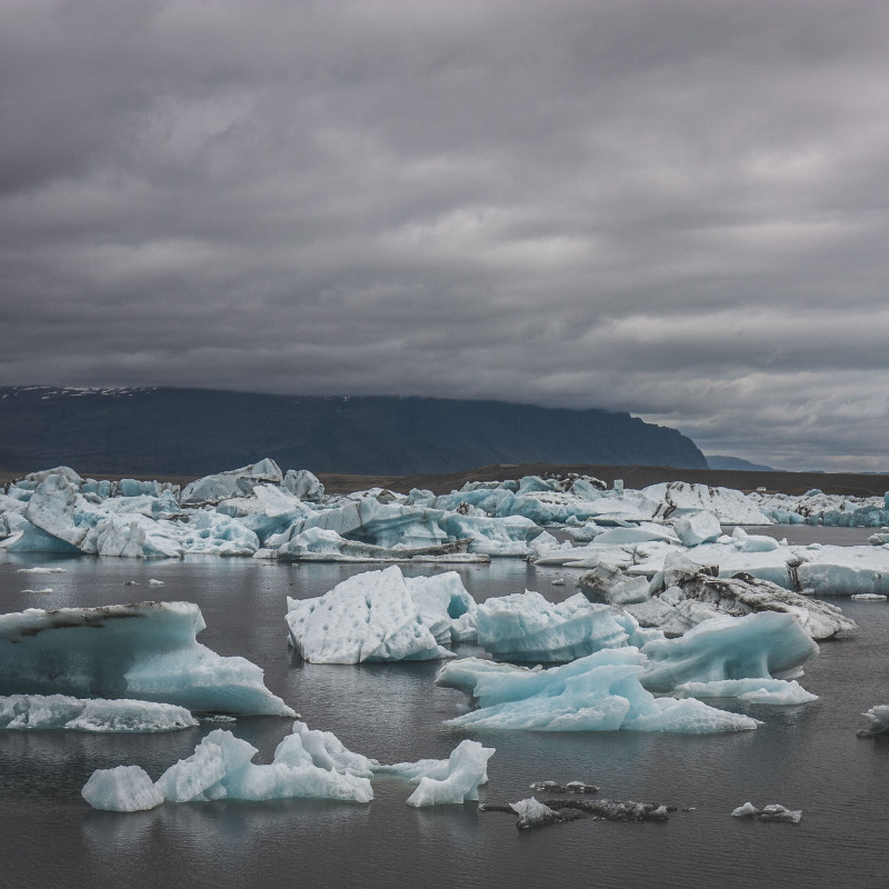 Eisschollen treiben im See, dichte Wolken am Himmel.