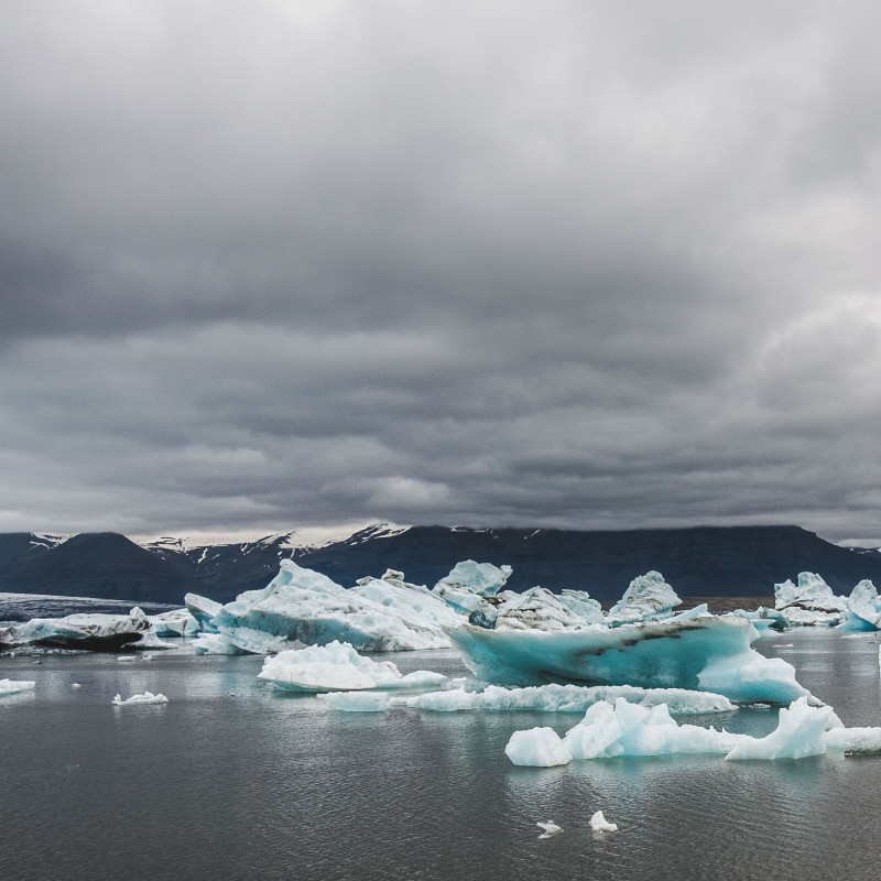 Eisschollen treiben im See, dichte Wolken am Himmel.