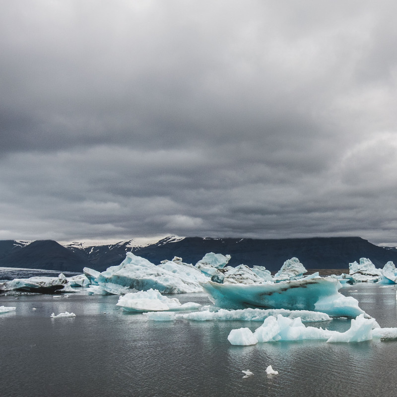 Eisschollen treiben im See, dichte Wolken am Himmel.