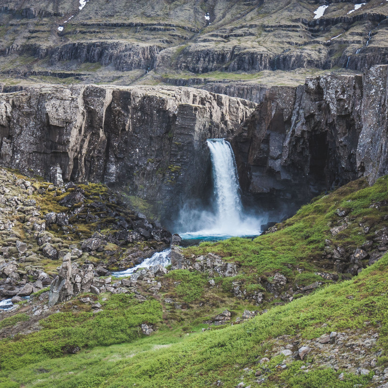 Ein Wasserfall bricht aus einer Felswand in Island.