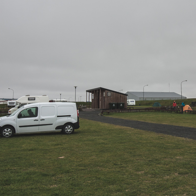 Weißer Campervan auf einem Campingplatz bei grauem Himmel.
