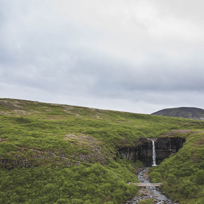 Grüne Landschaft, der Wasserfall erscheint winzig.