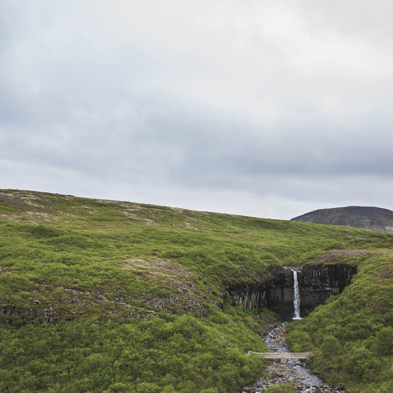 Grüne Landschaft, der Wasserfall erscheint winzig.