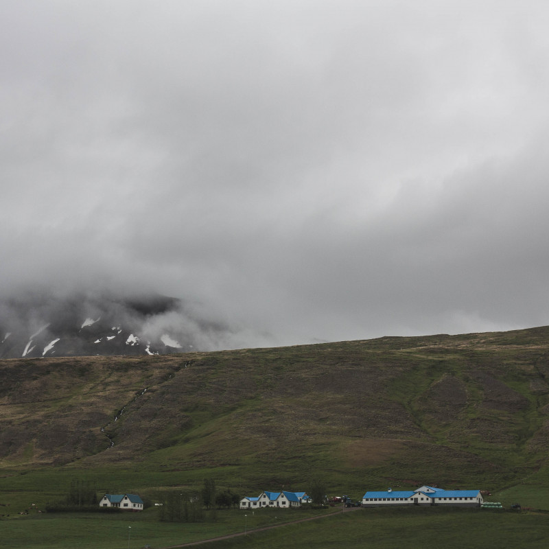 Häuser mit blauen Dächern, ein Hügel und im Nebel verschwindende Berge.