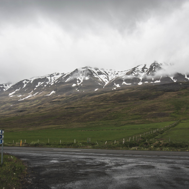 Straße, Weiden, schneebedeckte Berge in den Wolken.