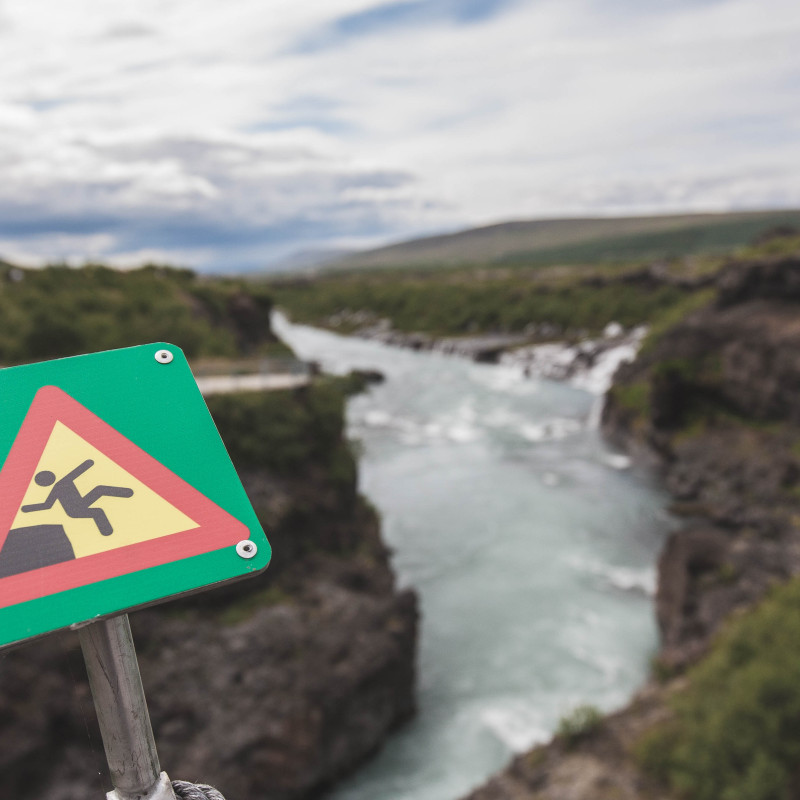 Warnschild vor der Klippe, Fluß im Hintergrund.
