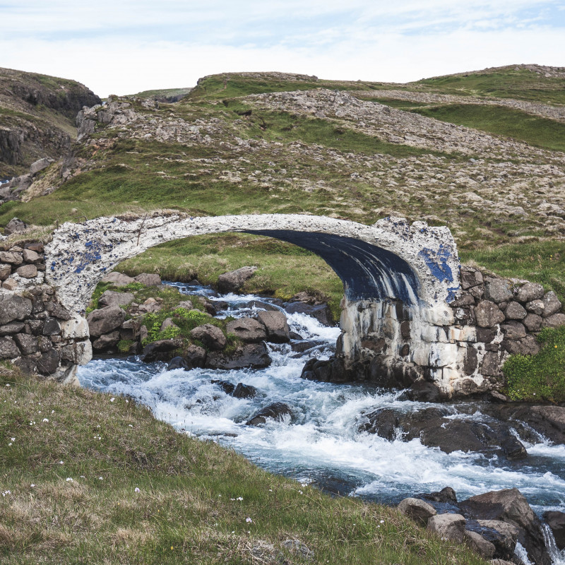Eine alte Brücke über einem wilden Wasserlauf.