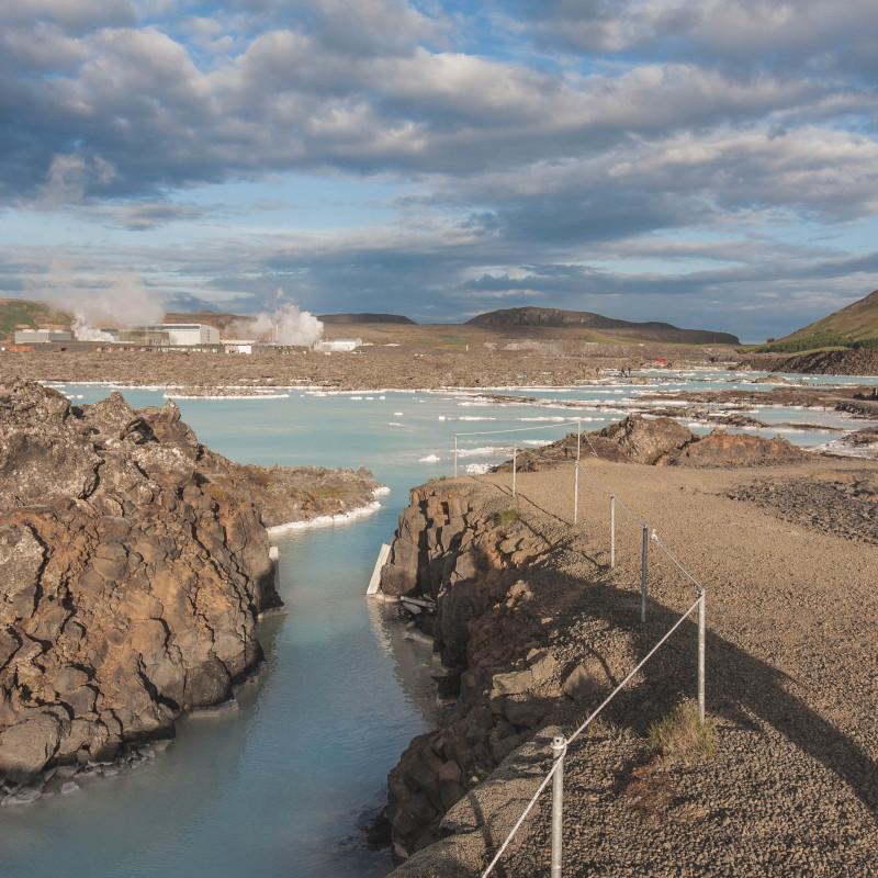 Ein Heizkraftwerk in der kahlen Landschaft Islands, im Vordergrund eine Wasserfläche.