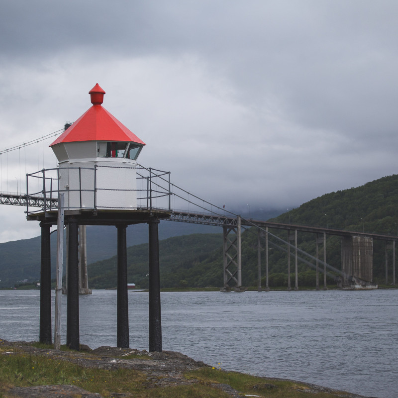 Ein kleiner Leuchtturm vor einer Brücke.
