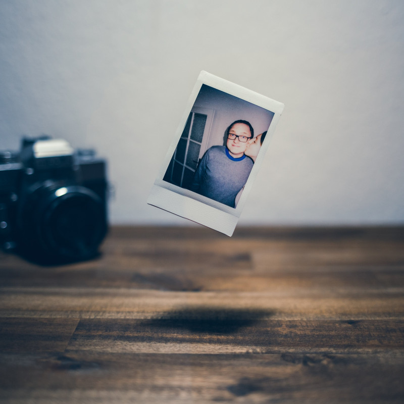 Ein Polaroid-Bild schwebt über dem Schreibtisch. Im Hintergrund eine Kamera.