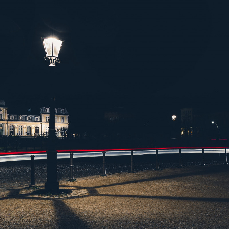 Eine Laterne bei Nacht, im Hintergrund die Lichtspur eines Autos.