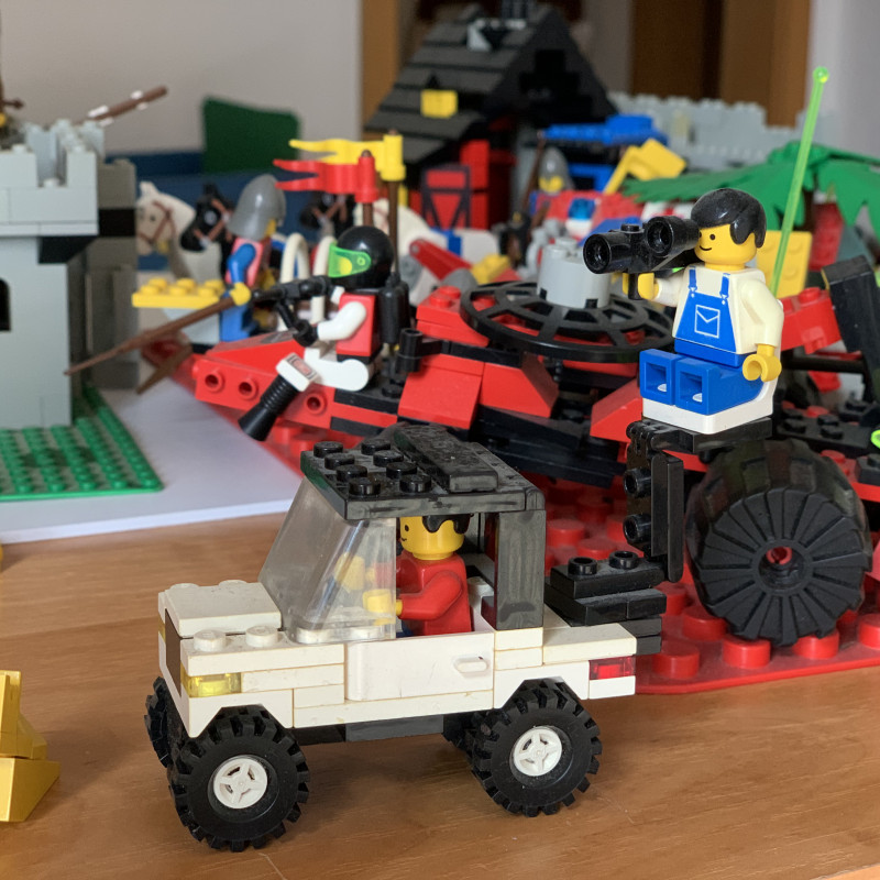 Ein kleines LEGO-Fahrzeug mit einem Mann und einer Kamera, im Hintergrund noch mehr Klemmbausteine.
