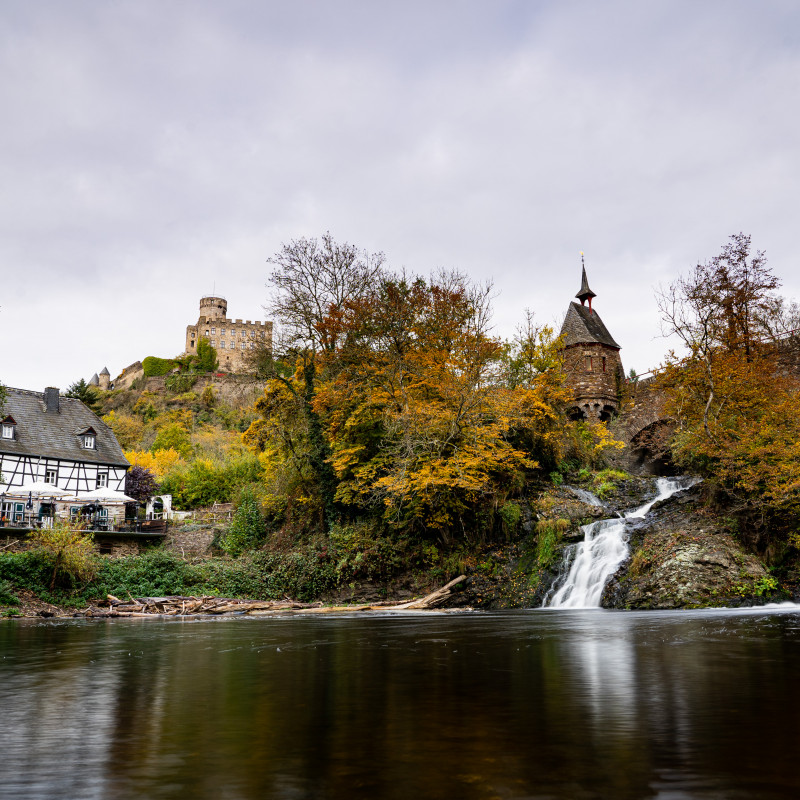 Ein altes Haus, eine Burg und ein Wasserfall unter einer Brücke.