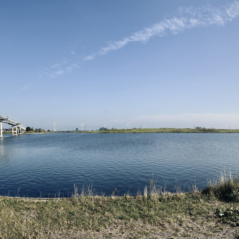 Panorama über einen See, am linken Bildrand eine Brücke.