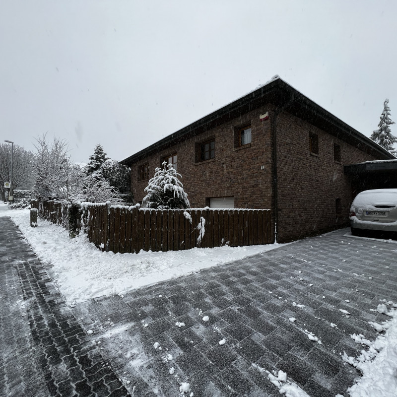 Die Ecke eines verschneiten Einfamilienhauses. Links eine Straße, rechts eine Einfahrt. Gehweg und Einfahrt sind geräumt.