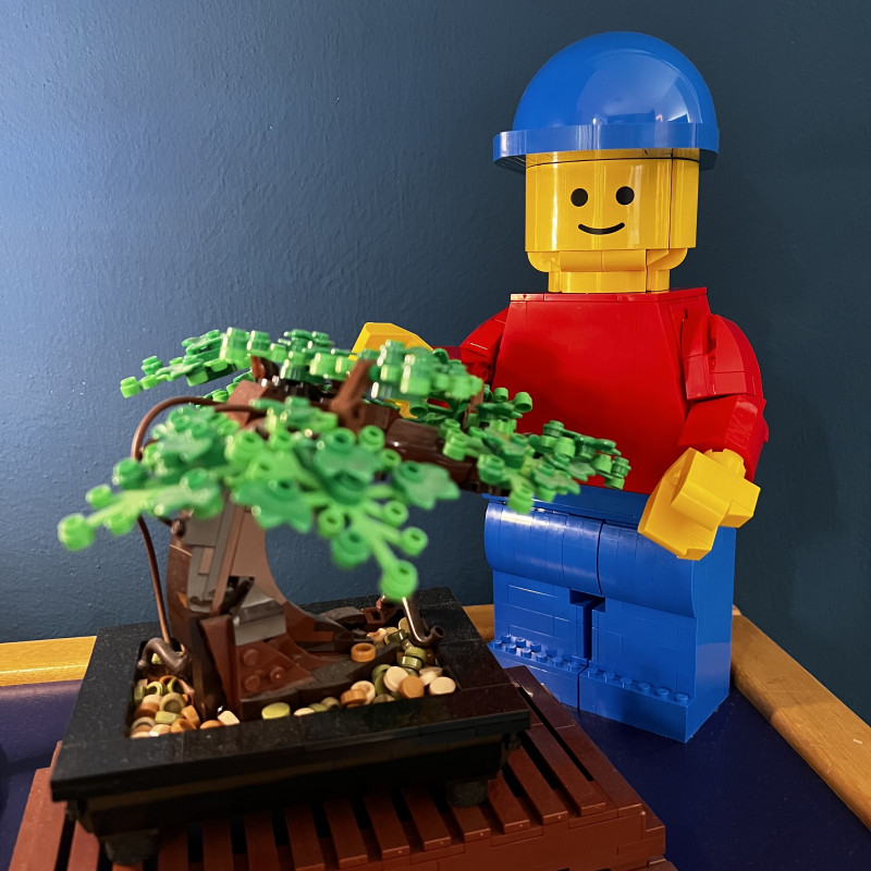 Eine große, aus Lego-Steinen gebaute Lego-Figur steht hinter einem aus Lego-Steinen gebauten Baum.