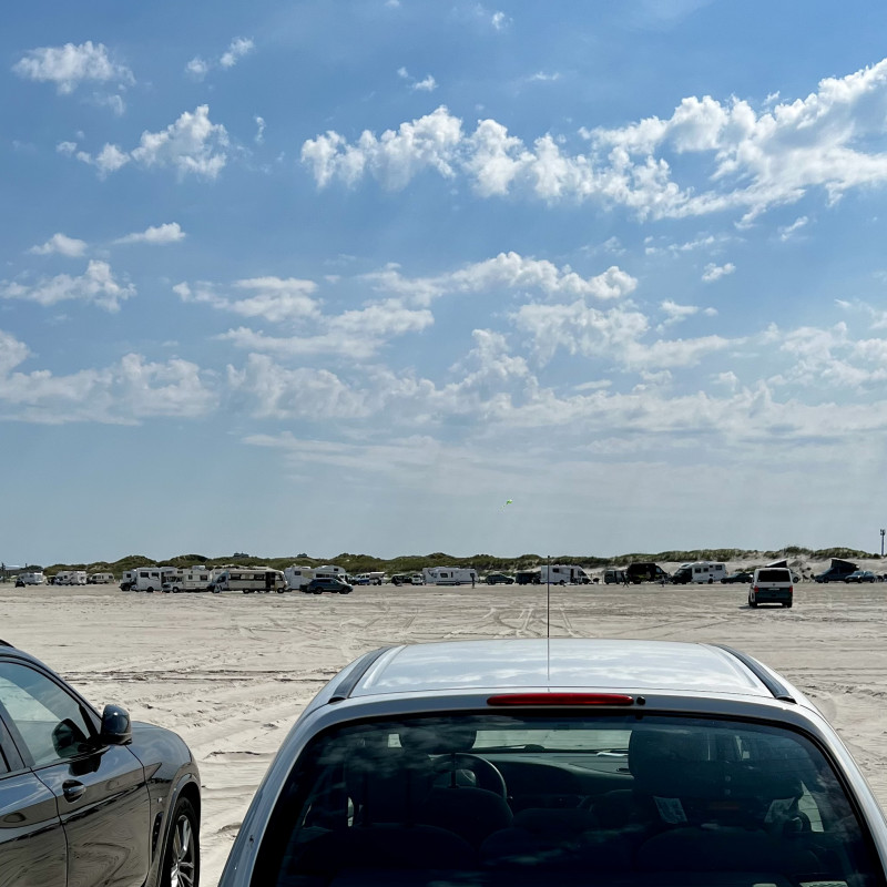 Autos parken unter blauem Himmel auf einem Sandstrand.