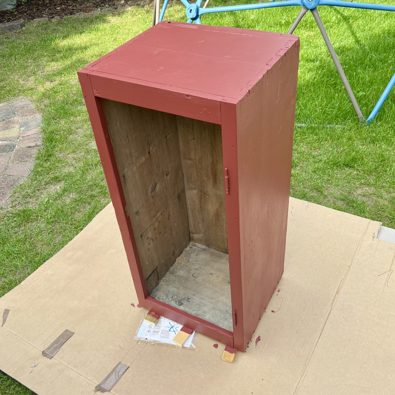 Ein frisch in "schwedenrot" lackierter Schrank ohne Tür steht auf einer großen Pappe.