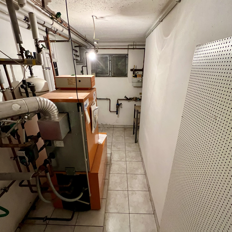 Eine orangene Gasheizung und allerlei Rohre und Kabel an Decke und Wänden.
