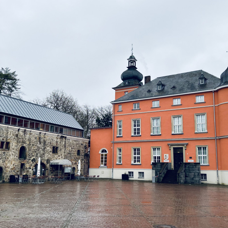 Ein leuchtend orangenes Haus in dem sich das Bilderbuchmuseum befindet. Links daneben ein altes Gemäuer mit modernem Dach.