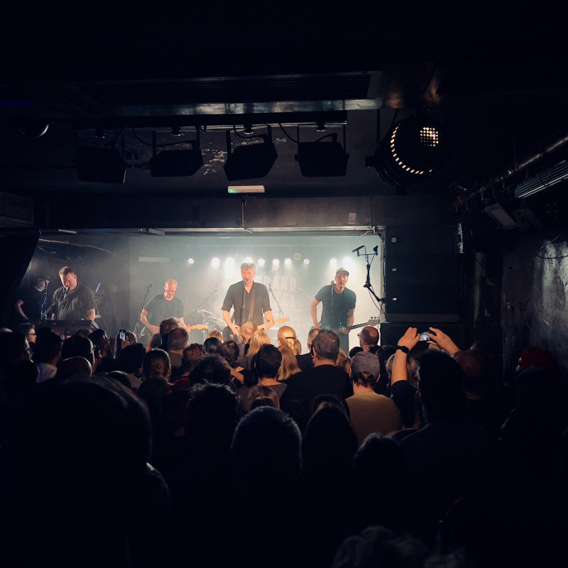 Die mit hellem Licht angestrahlt Band auf der Bühne, davor die Silhuette des Publikums.