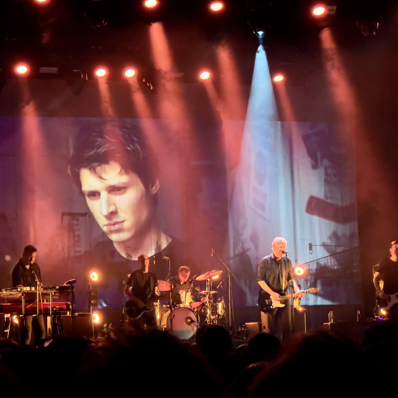 Die Band steht auf einer rot beleuchteten Bühne. Im Hintergrund wird das Musikvideo zu "Sommer '89" eingespielt, der Hauptdarsteller ist in Großaufnahme zu sehen.