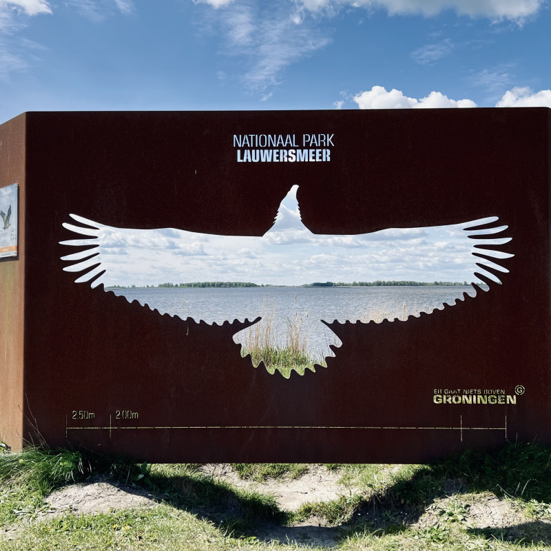 Die 2,5m breite Silhuette eines Greifvogels ist in eine Metalltafel geschnitten worden. Im Hintergrund ein Teil des Binnengewässers "Lauwersmeer".