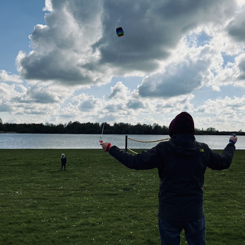 Ich lasse auf einer Wiese vor dem Wasser einen Drachen steigen. Am Himmel sind dicke Wolken.