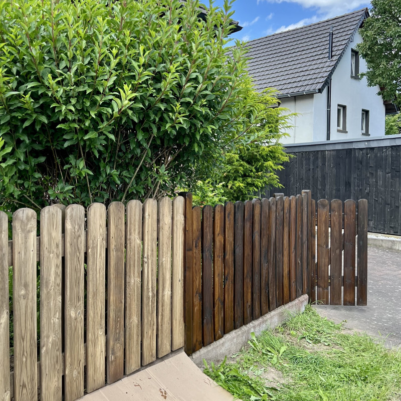 Ein Holzzaun dessen linke Hälfte noch vergraut aussieht. Die rechte Seite ist bereits in einem dunklen Braunton gestrichen.