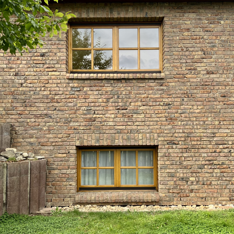 Zwei ordentlich gestrichene Fenster übereinander in einem verklinkerten Haus.