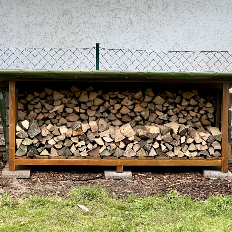 Ein Holzgestell mit gespaltenem Holz steht vor einem Maschendrahtzaun.