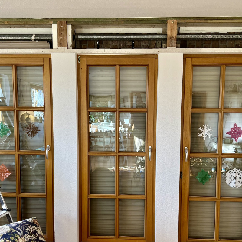 Drei hohe Fenster aus dem Raum heraus fotografiert, mit heruntergelassenem Rolladen und offenem Rolladenkasten. Rechts ist eine Leiter im Bild, im Fenster spiegelt sich der Autor.