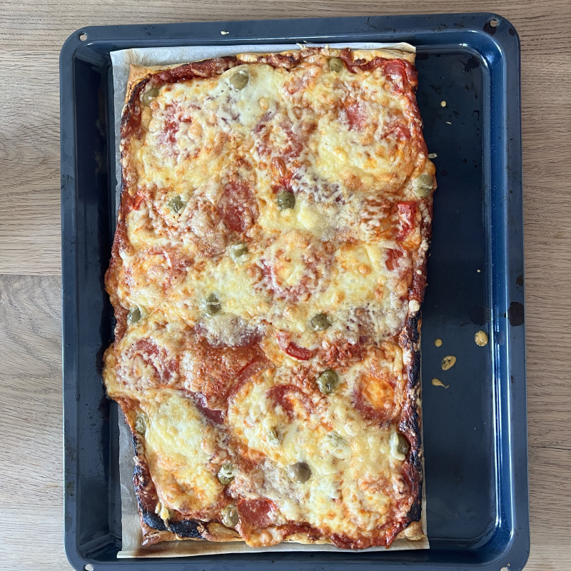 Eine Pizza mit Tomaten und Oliven auf einem großen Blech.